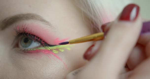 Die professionelle Visagistin trägt den rosa Eyeliner mit dem Pinsel auf das Gesicht der Frau auf. Bunt geschminkt. Rosa und Gelb. — Stockvideo