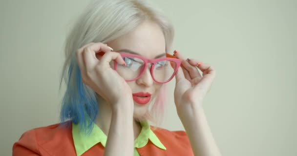 Portret pięknej blondynki z jasnym makijażem i kolorowymi włosami w różowych okularach i wysyłającej pocałunki na białym tle. Kobieta ma różowe i niebieskie oczy i — Wideo stockowe