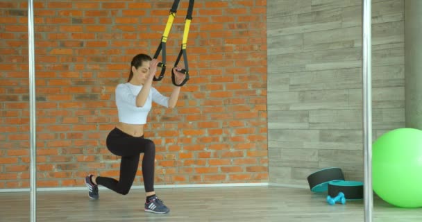 De aantrekkelijke magere vrouw doet lunges met de riemen in de sportschool. — Stockvideo