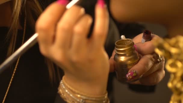Il make-up artist professionista sta applicando il rossetto lucido dorato con il pennello sul viso del modello afro-americano. Vista ravvicinata delle mani . — Video Stock