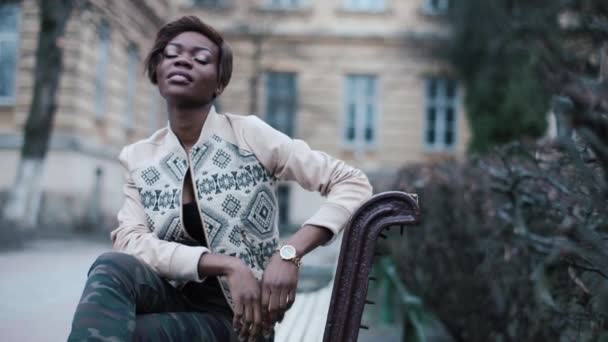 Piękne dopasowanie Afryki młoda kobieta z krótkimi włosami siedzieć na ławce na ulicy — Wideo stockowe
