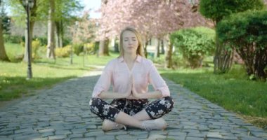 Genç sarışın kız parkta dinleniyor. Kadın nilüfer çiçeği pozunda meditasyon yapıyor. 4k görüntü.