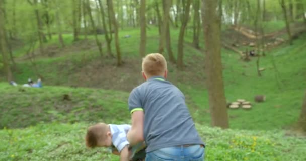 De lachende vader houdt zijn kleine lachende zoon vast en draait zich om in zijn armen. Bos locatie. 4k-beelden. — Stockvideo