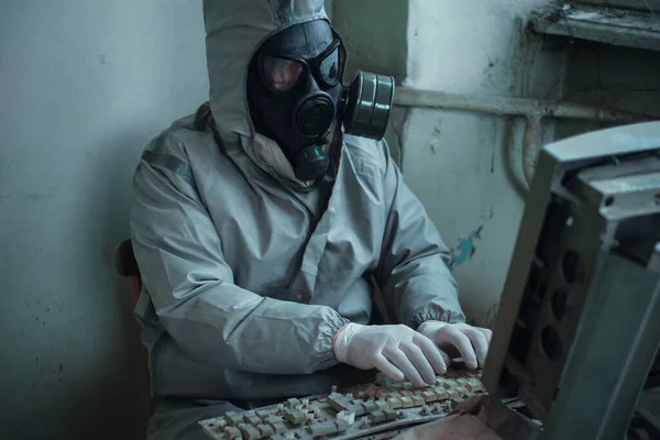 Scientist dosimetrist radiation supervisor in protective clothing and gas mask explores the danger zone. Sitting down on chair toward computer — Stock Photo, Image