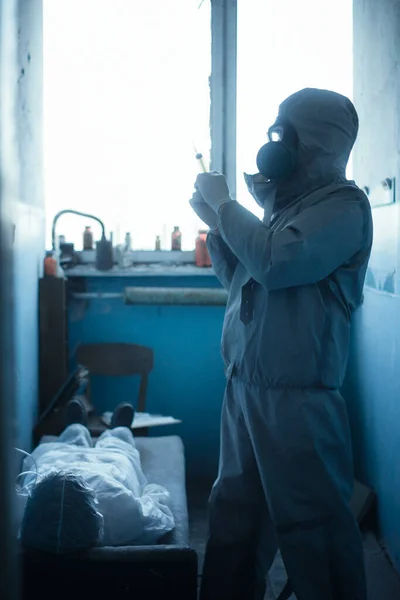 Scientist doctor in protective clothing and gas mask in danger zone. Doing injection for a patient