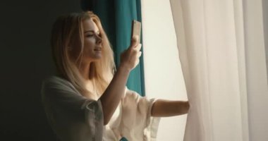 Çekici bir genç kadın, büyüleyici gülüşü ve sarı saçlarıyla güneşin doğuşunun fotoğrafını çekiyor. 4k görüntü.