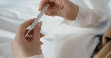 Termometreyi tutan kadın ellerinin yakın görüntüsü. Bilinmeyen kadın yatakta yatarken vücut ısısını kontrol ediyor..