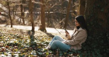 Sonbahar bahar titreşimleri. Rüzgâr kadınların saçlarını savururken o da akıllı telefonunda parkta oturmuş bir şeyler okuyor.