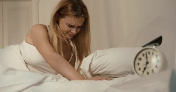Cansada mujer enojada está cerrando sus oídos con la almohada. Está apagando el despertador y volviendo a la cama. 4k. — Vídeo de stock