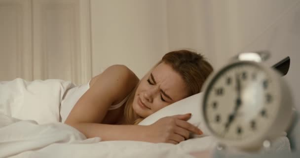 Bedårande trött kvinna är arg bacause av väckarklocka på morgonen. Hon stänger öronen med kudden. 4k-bilder. — Stockvideo