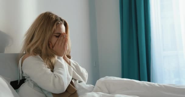 Retrato lateral de la mujer rubia enferma estornudando y sonándose la nariz mientras está acostada en la cama. Imágenes de 4k. — Vídeo de stock
