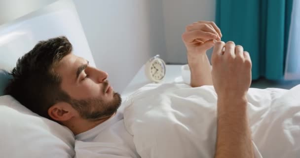 Oldalnézet a beteg ember ellenőrzi a testhőmérsékletét a hőmérővel. Az ágyban pihen. 4k felvétel. — Stock videók