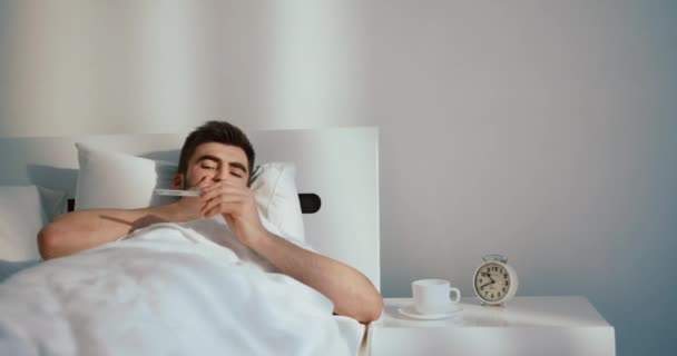 Хвора людина з холодом відпочиває в ліжку і перевіряє температуру тіла за допомогою термометра. 4k кадри . — стокове відео