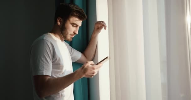 Boczny portret pewnego siebie mężczyzny rozmawiającego poważnie przez telefon komórkowy przy oknie. Poranna koncepcja. Wschód słońca. 4k. — Wideo stockowe