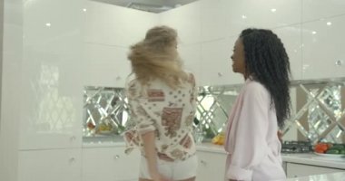 İki güzel, mutlu, etnik çeşitlilikte esmer ve sarışın kız arkadaş modern mutfakta dans ederken eğleniyorlar. Sabah konsepti.