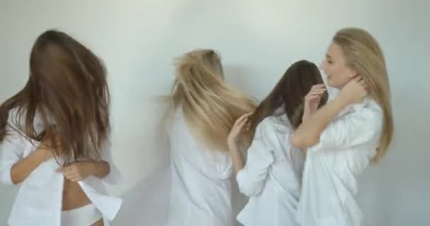 Fyra attraktiva flicka vänner med naturlig make-up har roligt samtidigt skaka sin långa naturliga blont hår på vit bakgrund. De har vita byxor och skjortor.. — Stockvideo