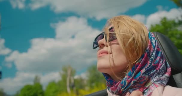 Porträt einer hinreißend modischen blonden Frau, die im Cabrio fährt. Sie trägt Sonnenbrille und Schal auf dem Weg von den windblonden Haaren. 4k Filmmaterial. — Stockvideo