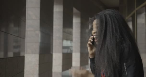 Emocionální portrét rozkošné africké dívky, která se směje přes mobilní telefon na ulici. Záběry 4k. — Stock video