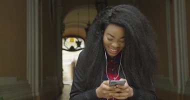 Güzel gülüşlü tatlı Afrikalı genç kız, açık cep telefonuyla internette mesajlaşırken ve internette gezinirken şaşırdığını ifade ediyor..