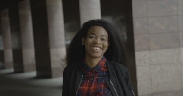 Veselá usmívající se africká dívka radostně sestupuje po schodech ke kameře. 4k záběry. Přední venkovní portrét. — Stock video