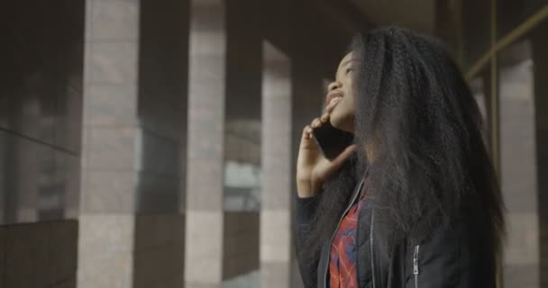 Boční portrét půvabné afro-americké dívky s hezkým úsměvem smějící se při rozhovoru přes mobilní telefon venkovní. — Stock video