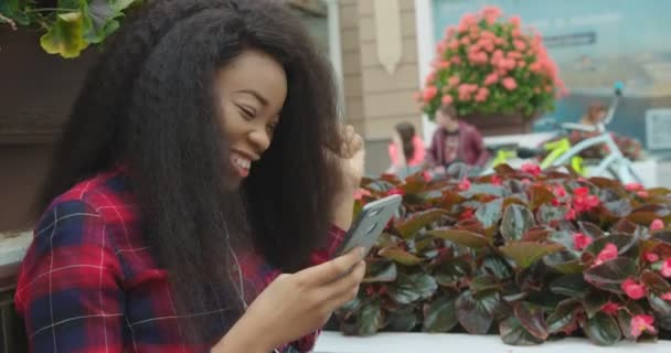 Emotionele Portret Charmant jong Pretty AFrican meisje Luisteren Muziek Oortelefoons sms 'en Chatten Browsen Mobiele telefoon One Outdoor 4k Genieten Grappig. — Stockvideo