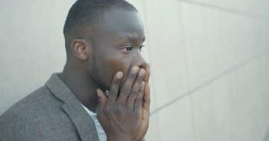 Çaresizlik içindeki yakışıklı Afrikalı adam. Mutsuz adam duygusal olarak başını kaşıyor. Yan portre. 4K görüntü. Açık hava..
