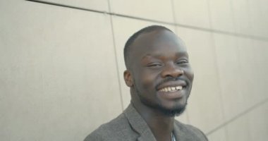 Mutlu yakışıklı Afro-Amerikalı adam duygusal olarak gülüyor ve beyaz kapının yanındaki kameraya bakıyor. 4K içinde yakın plan portre.