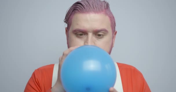 Roze hoofd jongeman blaast de blauwe ballon en zijn emoties op als het knalt. Studio locatie. — Stockvideo