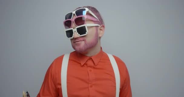 Atraktivní mladý retro muž s růžovými vlasy. vousy a tři páry slunečních brýlí má, zatímco tančí na bílém pozadí. Záběry 4k. — Stock video