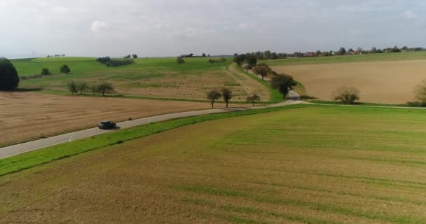 Drönaren följer körbilen längs den smala vägen i vackra soliga gyllene fältet på tyska. — Stockvideo