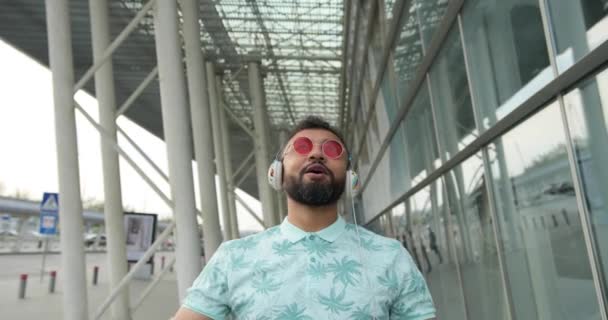 Ο συναισθηματικός Αφρικανός χαίρεται υψώνοντας τα χέρια κοντά στο αεροδρόμιο. 4k πλάνα. Απολαμβάνει τη μουσική με ακουστικά.. — Αρχείο Βίντεο