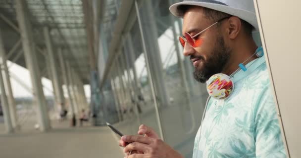 Retrato de close-up lateral do pronto para férias homem africano feliz conversando e navegando no telefone celular perto do aeroporto. Filmagem 4k. — Vídeo de Stock