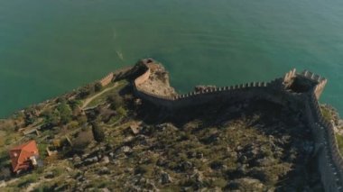 Alanya kalesinin kayalık tepelerdeki eski duvarları üzerinde hava aracı uçuşu ve Akdeniz tarafından aşırı yıkanma. Yavaş çekim, 4k.