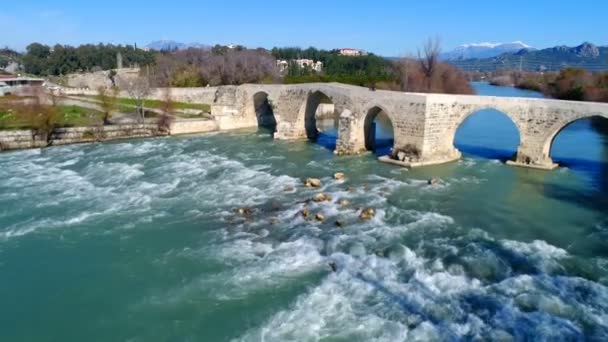 Antalya tartomány, Törökország. Nyáron. A helikopter átrepül az ősi történelmi Seljuk hídon, amit az Eurymedon folyó felett emberek borítanak. Elbűvölő látványosság. 4k. — Stock videók