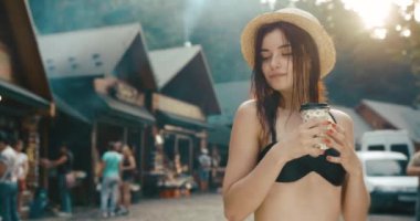 Islak saçlı hayalperest genç kadın, dağlarda bir yerlerde bikinili bir şekilde yürürken kahve içiyor.