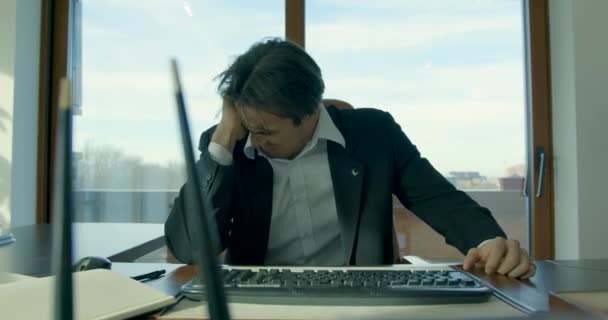 Concepto de crisis empresarial. Un joven empresario sentado en la mesa de la oficina. Hombre de traje interior sobre fondo de ventana de vidrio. — Vídeos de Stock