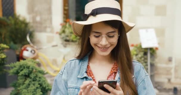 Genç kız ve teknoloji. Genç kadın eski şehirde bir yerde duruyor ve bir şeyler okuyor ya da akıllı telefonundan sosyal ağları kontrol ediyor. — Stok video