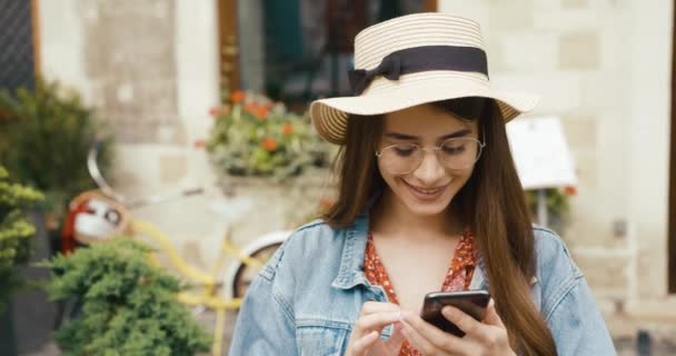 Ragazza e tecnologia. Giovane donna si trova da qualche parte nella città vecchia e legge qualcosa o controlla i social network nel suo smartphone — Video Stock