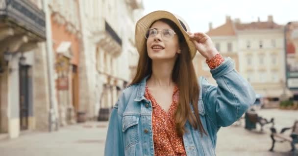 Turista femenina en el casco antiguo europeo. Chica mira hacia arriba en la hermosa arquitectura y sostiene su sombrero encantador — Vídeos de Stock