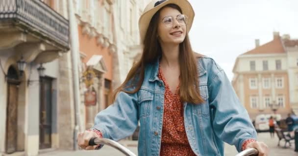 Jovem turista fermacho na antiga cidade europeia. Jovem encantadora em vestido vermelho caminha com uma bicicleta e olha em volta para a bela arquitetura — Vídeo de Stock