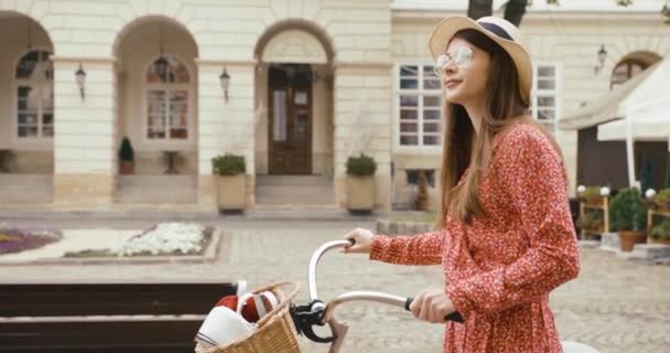 Jovem turista fermacho na antiga cidade europeia. Jovem encantadora em vestido vermelho caminha com uma bicicleta e olha em volta para a bela arquitetura — Vídeo de Stock