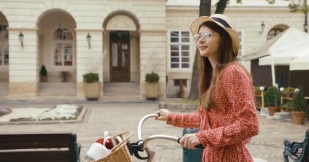 Mladý fermale turista ve starém evropském městě. Okouzlující mladá žena v červených šatech procházky s jízdním kolem a rozhlíží se po krásné architektuře — Stock video