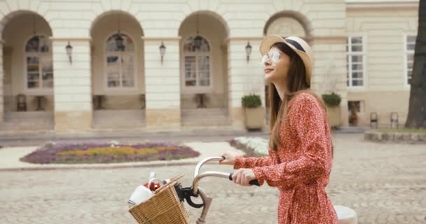 Jovem turista fermacho na antiga cidade europeia. Jovem encantadora em vestido vermelho caminha com uma bicicleta e olha em volta para a bela arquitetura — Vídeo de Stock