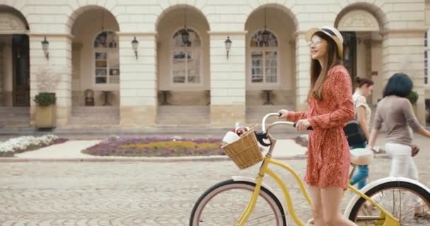 Fiatal ferman turista a régi európai városban. Bájos fiatal nő piros ruhában sétál egy kerékpárral, és körülnéz a gyönyörű építészet — Stock videók