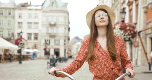 Jovem turista fermacho na antiga cidade europeia. Jovem encantadora em vestido vermelho caminha com uma bicicleta e olha em volta para a bela arquitetura — Vídeo de Stock