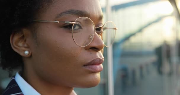 4k. Zeitlupe. Nahaufnahme einer charmanten, ernsthaften Afroamerikanerin mit Brille, die vor einer Glaswand im Freien steht — Stockvideo