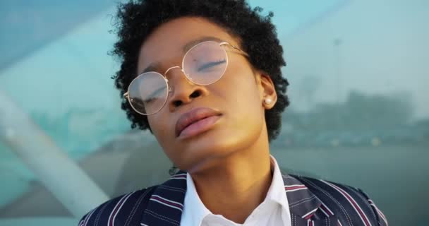 4k. Αργή κίνηση. Αφρο-Αμερικανίδα επιχειρηματίας με κομψό ριγέ κοστούμι κοιτάζει το ρολόι της και στέκεται ανήσυχος μπροστά σε ένα σύγχρονο κτίριο — Αρχείο Βίντεο