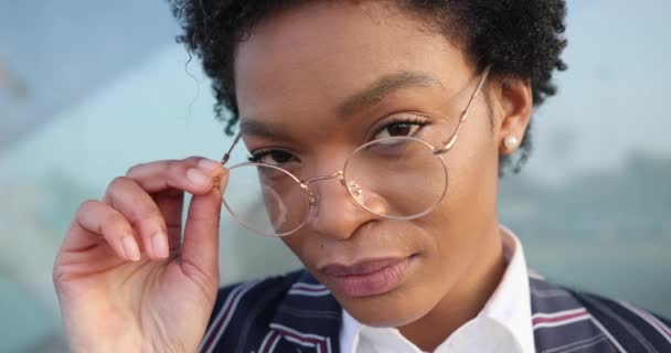 4k. Αργή κίνηση. Πορτρέτο της όμορφης Αφρο-Αμερικανίδας που βγάζει τα χρυσά της γυαλιά ενώ στέκεται μπροστά σε ένα σύγχρονο κτίριο έξω — Αρχείο Βίντεο