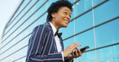 4 bin. Seyahat et, Dijital. Modern giyinmiş Afro-Amerikalı çekici kadın cam duvarın yanında duruyor ve telefonunda bir şeyler okuyor. İş kadını ya da öğrenci